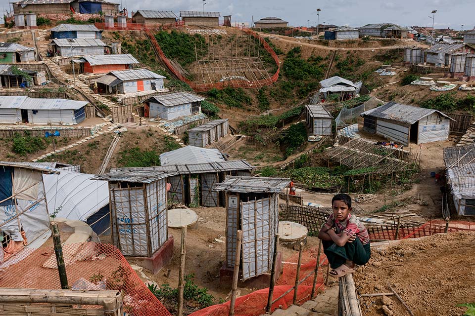 a child sits atop a fence overlooking a Rohingya refugee camp in Bangladesh