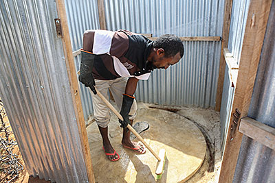 Hygiene promoter Ahmed Hussein disinfects his family's latrine in the world's largest refugee camp: Kambioos in Dadaab, Kenya. Photo by Sara A. Fajardo/CRS