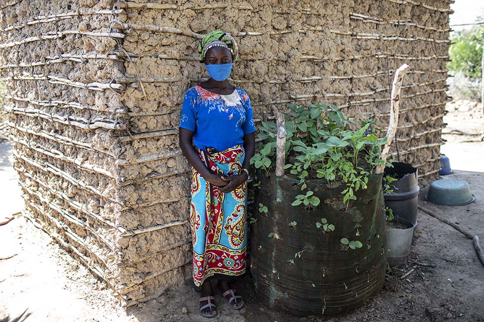 Kenya woman stands outside her home near her small garden