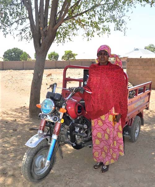 Nigerian woman standing near her motorized tricycle.