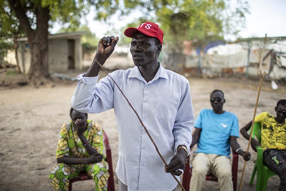 South Sudanese man holding a stick and speaking to a group