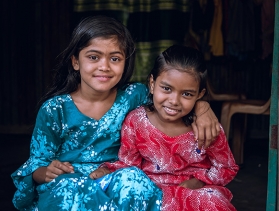 Two Bangladeshi young girls smile and sit together with their arms around each other  