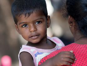Little boy from Sri Lanka looks at camera while in mother’s arms